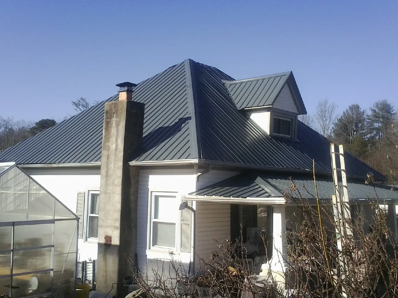 Dark blue standing seam metal roof on a white farmhouse with dormer — Slate & Tile Roof Repair by Roofing Brothers in Rocky Ridge