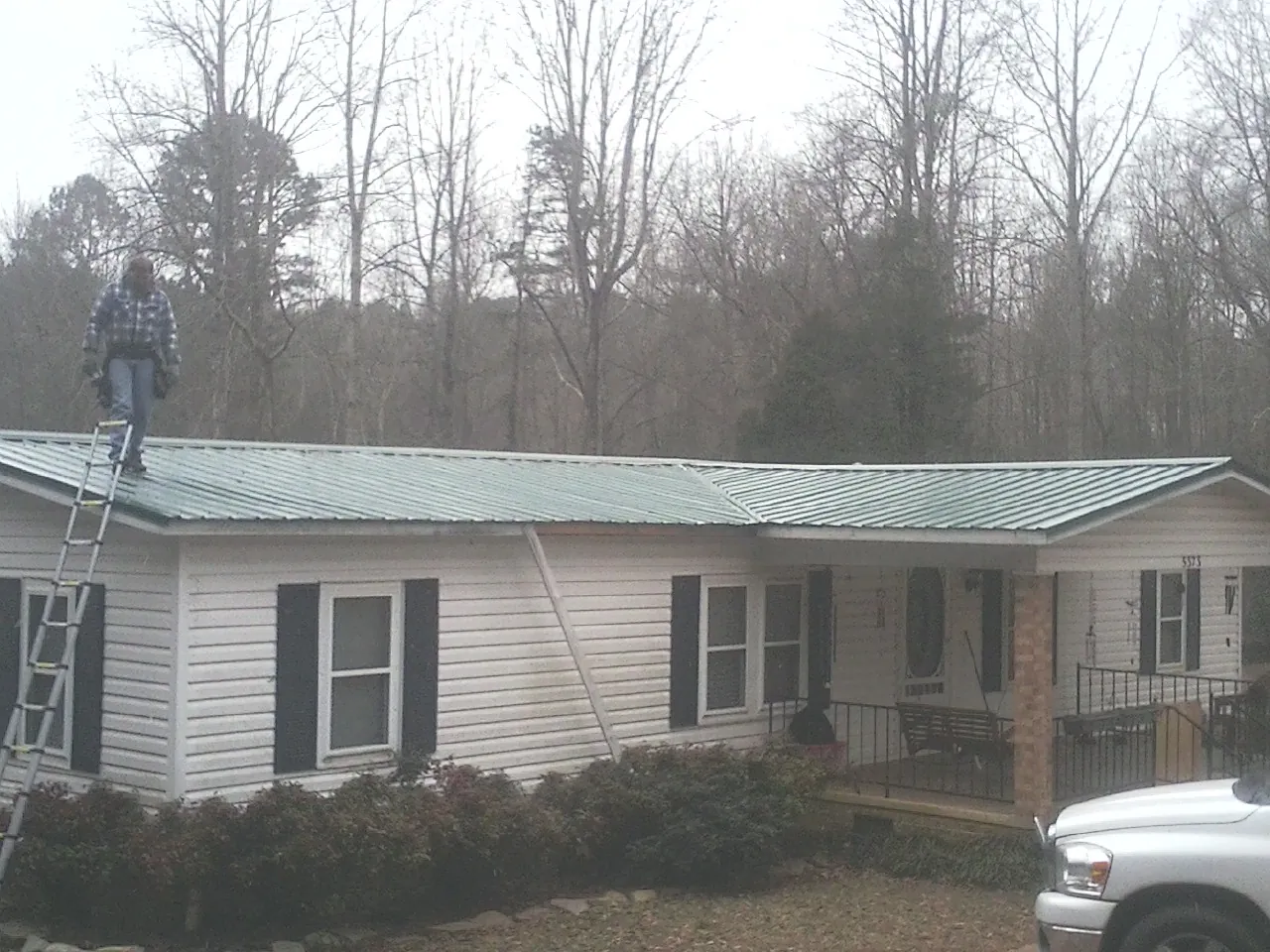 Worker on a ladder beside a new green metal roof on a ranch home in Rocky Ridge