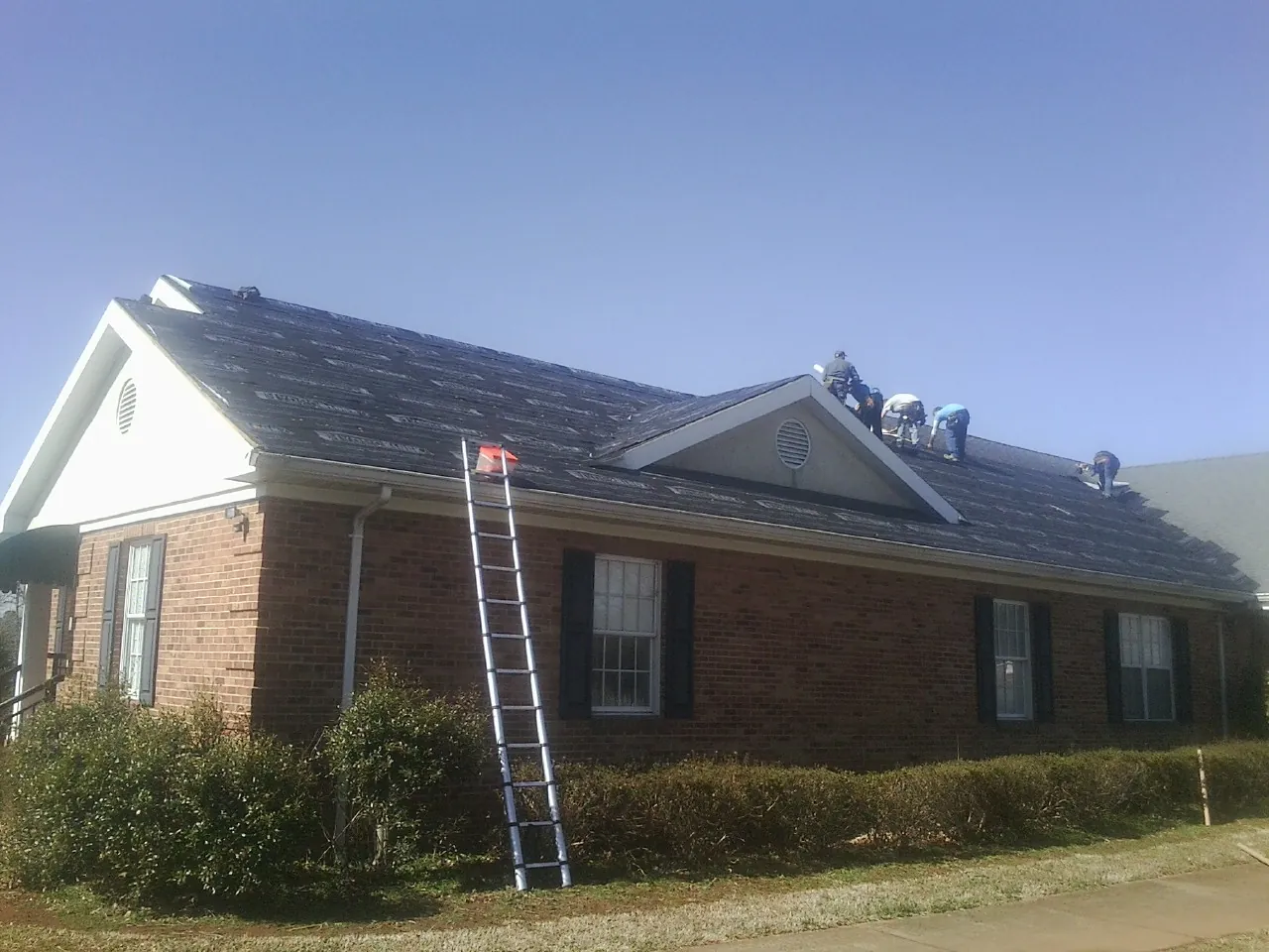 Crew tearing shingles off a brick ranch roof with a ladder set — Metal Roof Repair work by our crew in Rocky Ridge