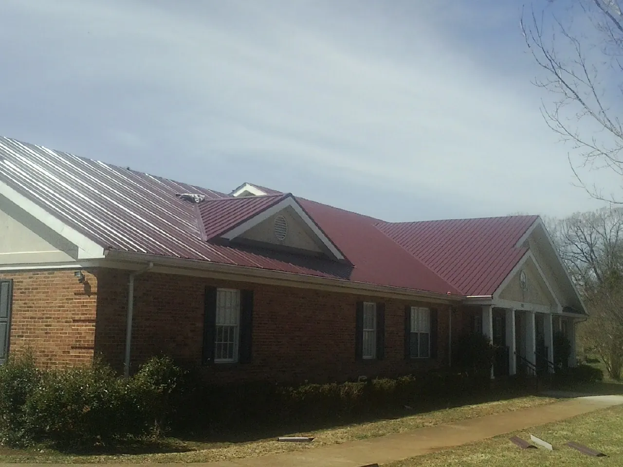 Red metal roof with gabled entries on a long brick building, from a Hail Damage Roof Repair job in Rocky Ridge