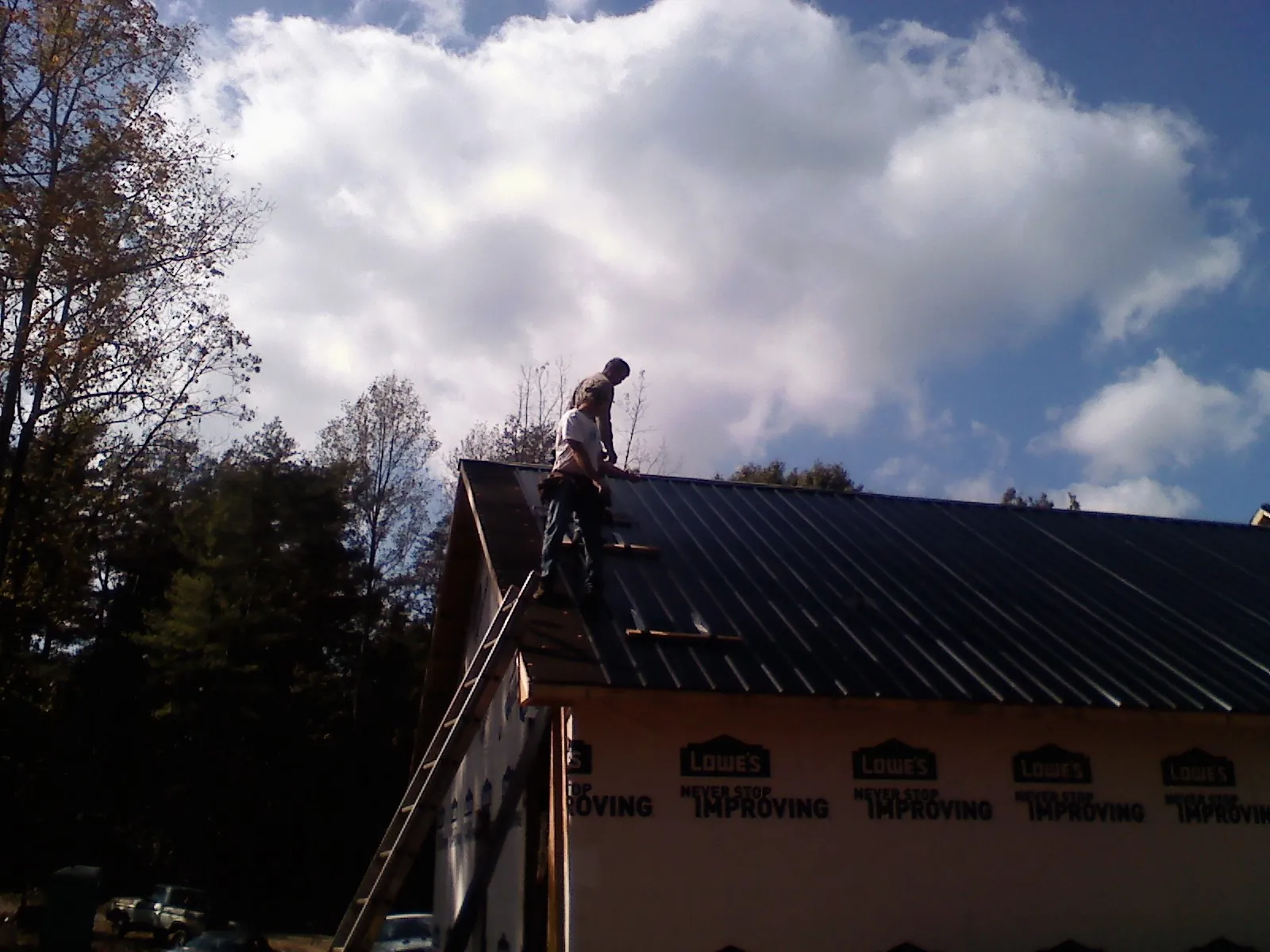 Roofer fastening dark metal panels high against a cloudy sky, from a Roof Inspection job in Rocky Ridge