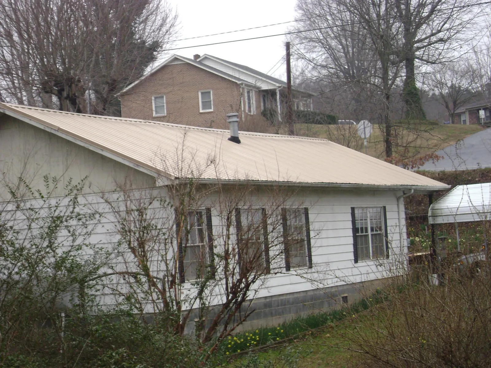 Tan metal roof on a white sided house set into a hillside — Commercial Roofing by Roofing Brothers in Rocky Ridge