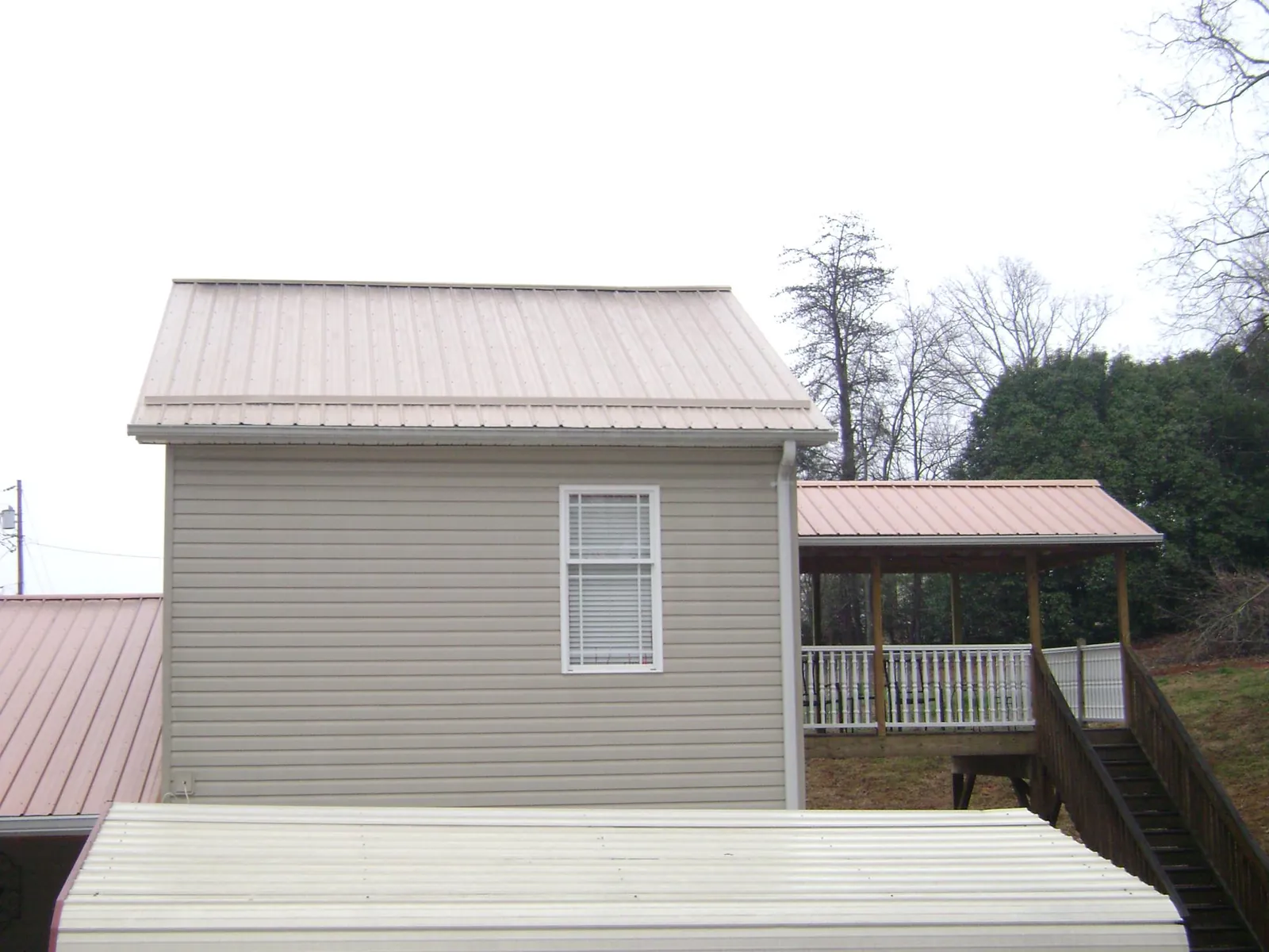 Tan metal roofs on a two story addition and attached porch, from a Roof Replacement job in Rocky Ridge